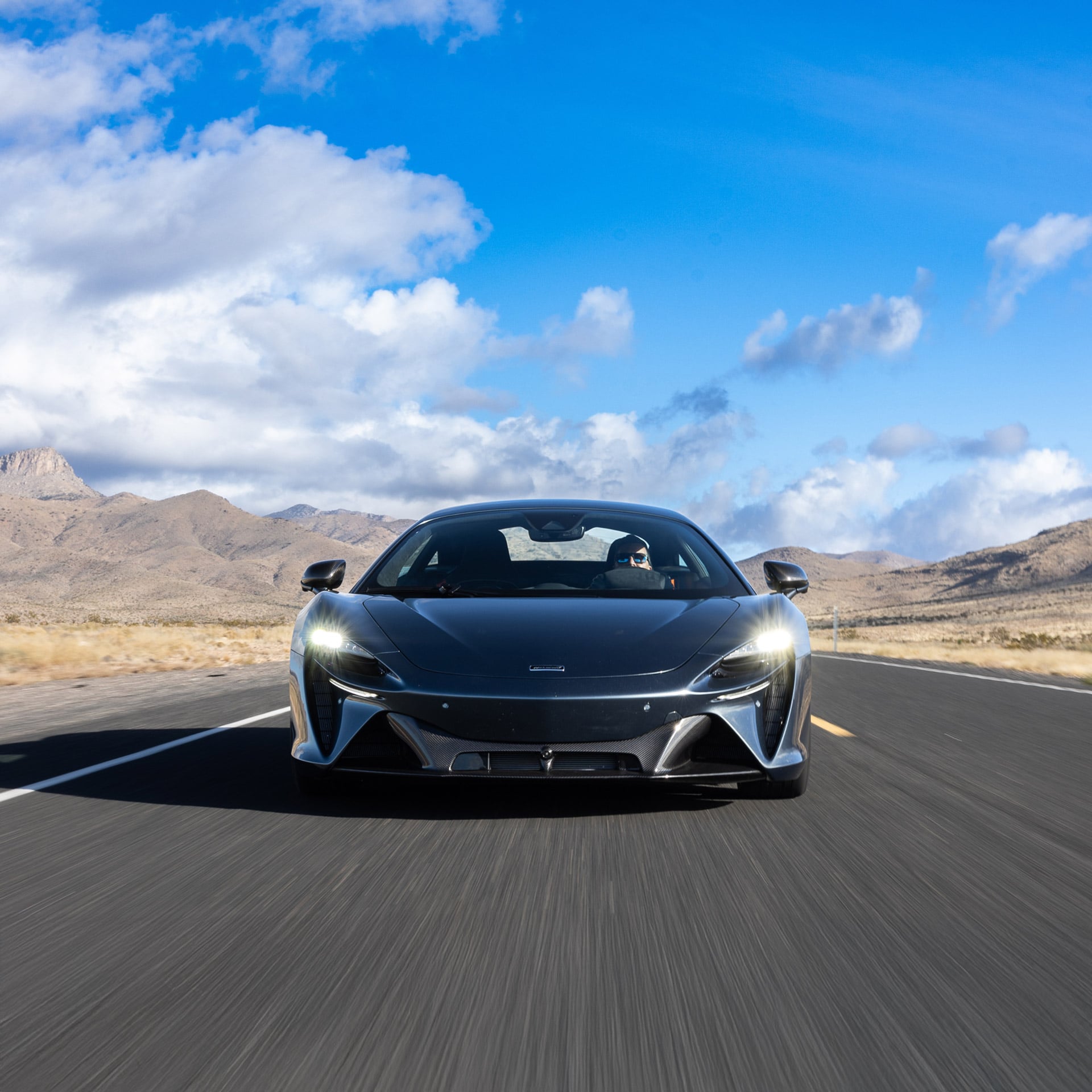 McLaren Artura plug-in hybrid supercar in orange, low angle front view on a racetrack